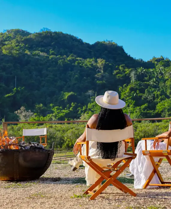 Two women in flowy white skirts relaxing by the campfire at The Stables at Sleeping Giant.